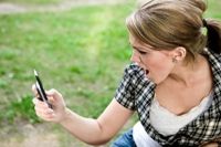Photo of a girl looking angry and shocked by a text on her cell phone.